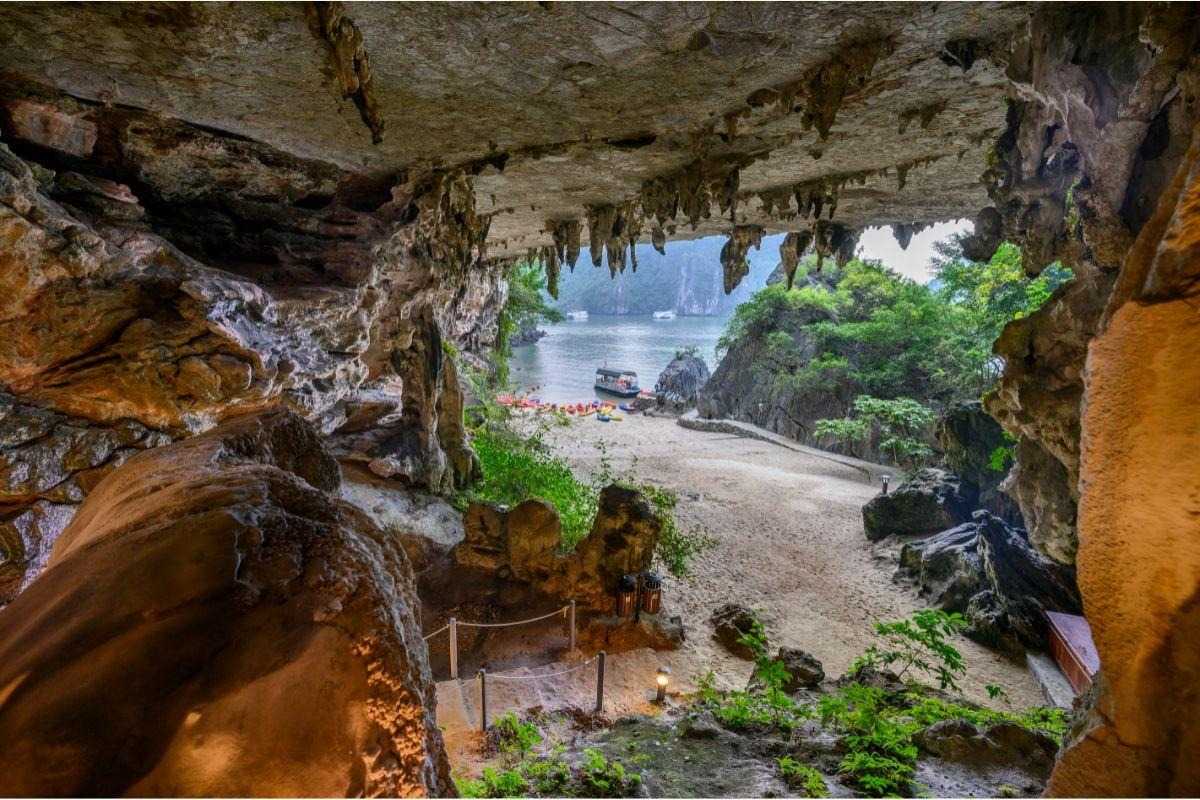 Me Cung Cave Halong Bay scenic cave entrance view Me Cung Cave Halong Bay shows a rocky cave entrance overlooking the sandy shore and boats on the bay.