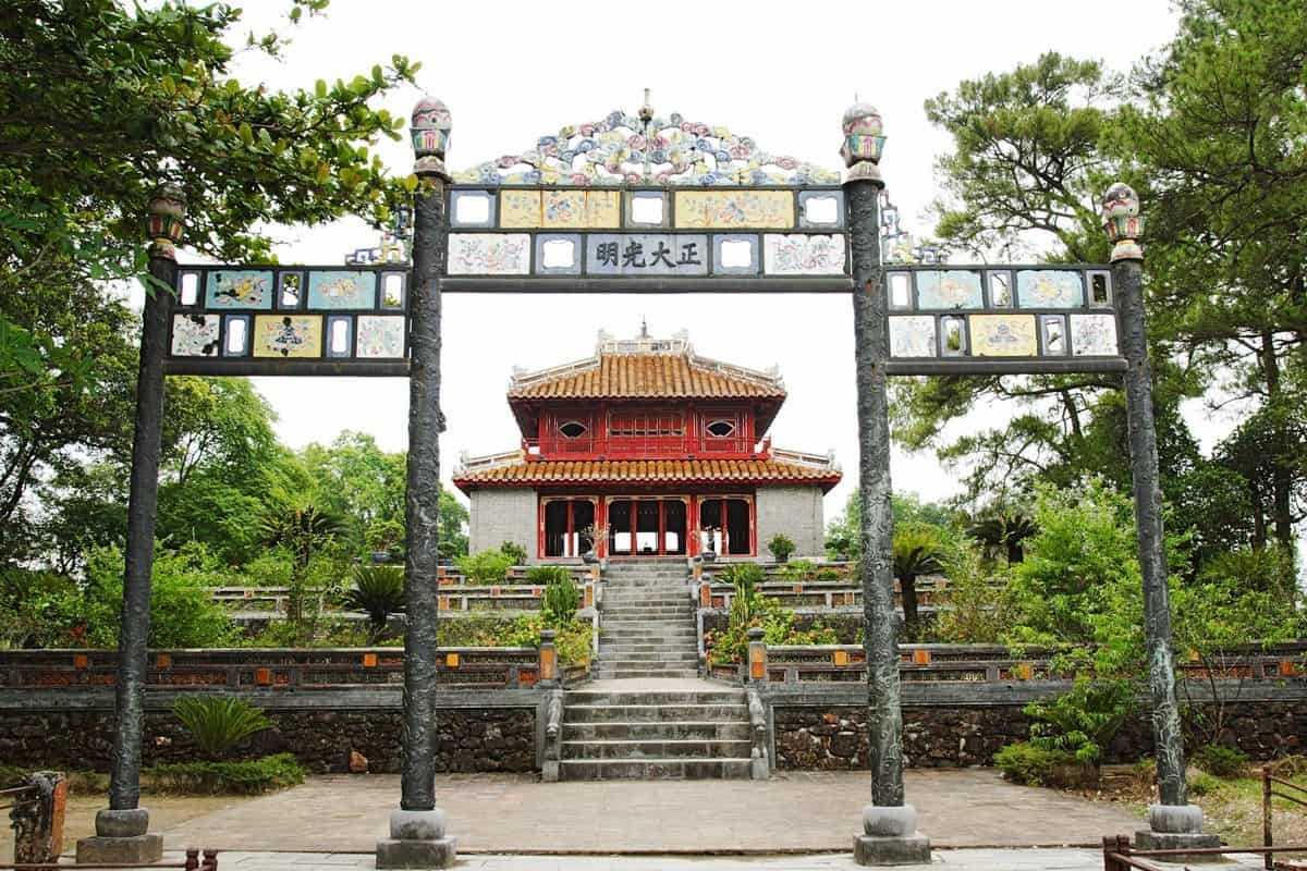 Imperial Gardens and Causeway at Minh Mang Tomb Expansive garden and tiled causeway leading to Minh Mang Tomb’s grand gate in Hue, lined with lush plants and palm trees.
