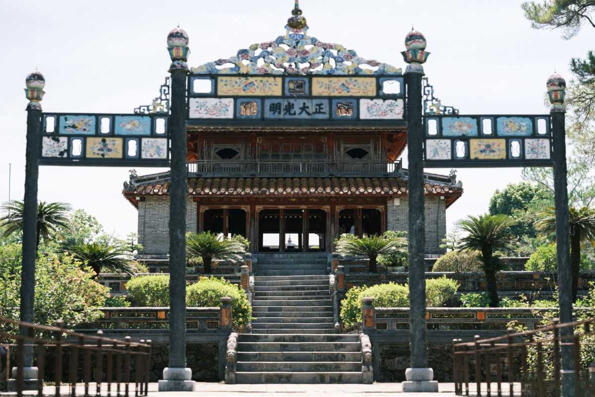 Sunlit Mosaic Gate at Minh Mang Tomb, Hue Mosaic-decorated gate at Minh Mang Tomb Hue with intricate imperial motifs, illuminated by soft morning sunlight and surrounded by greenery.