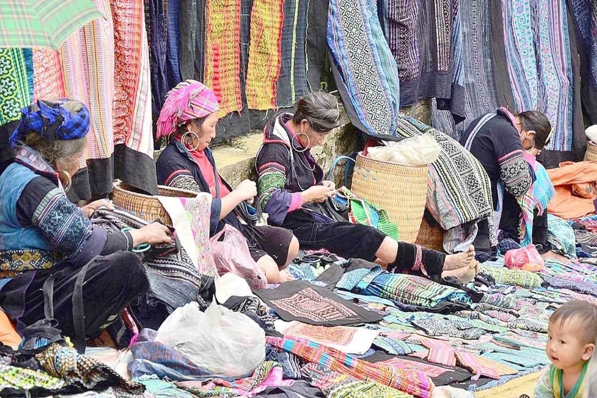 Muong Hum Market Sapa handmade textiles artisans at work Muong Hum Market Sapa artisans create handmade textiles with colorful patterns, showcasing traditional skills.