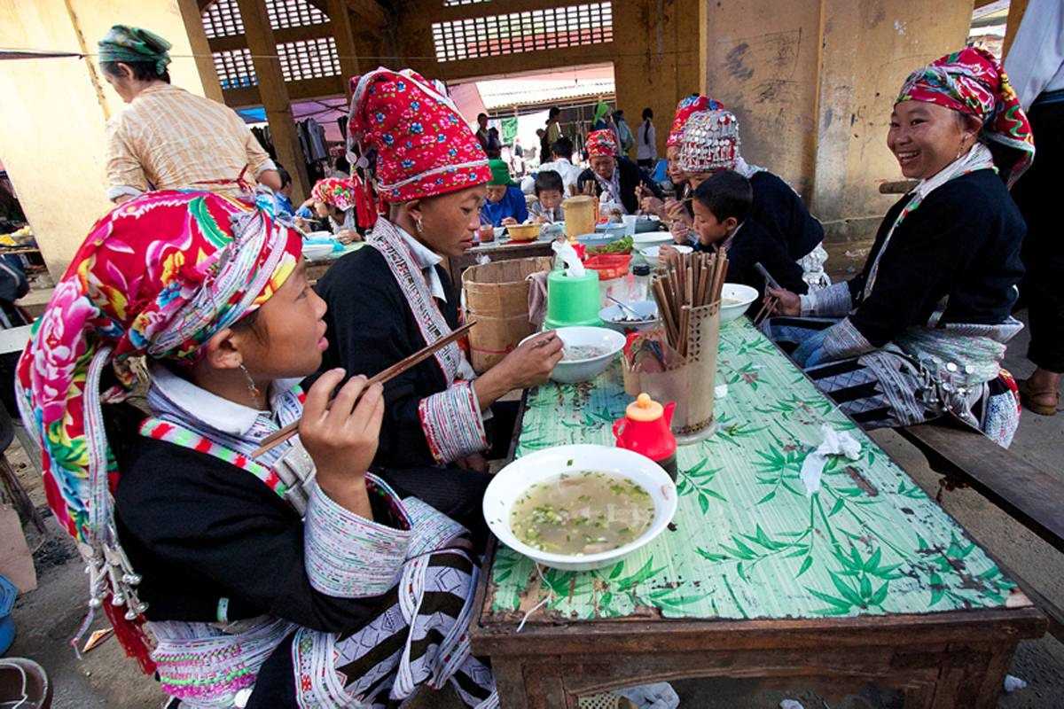 Muong Hum Market Sapa Red Dao families sharing a meal Muong Hum Market Sapa features Red Dao families enjoying traditional meals together in the busy food court area.