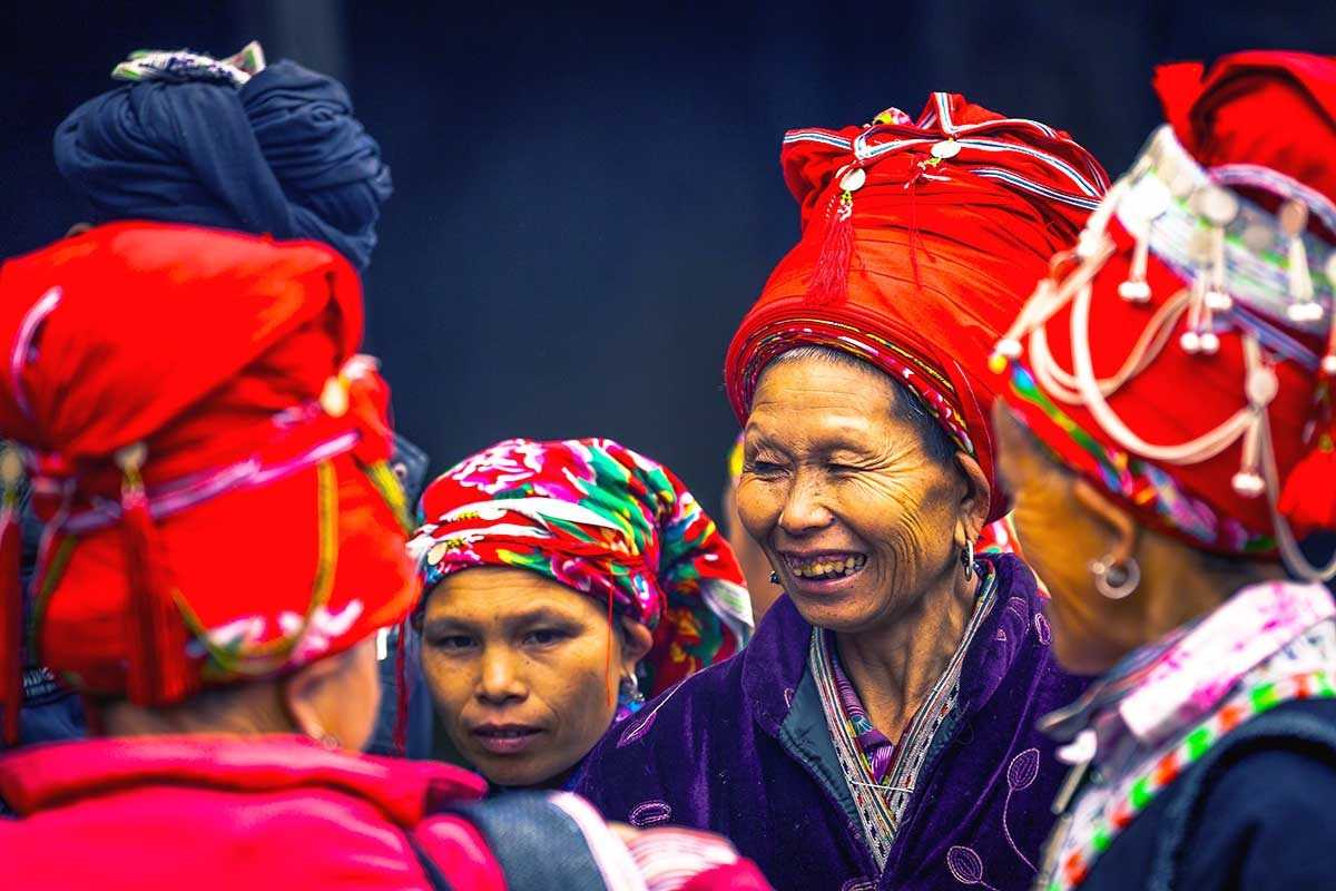 Muong Hum Market Sapa Red Dao women cultural gathering Muong Hum Market Sapa highlights vibrant Red Dao women socializing in traditional attire during the busy market day.