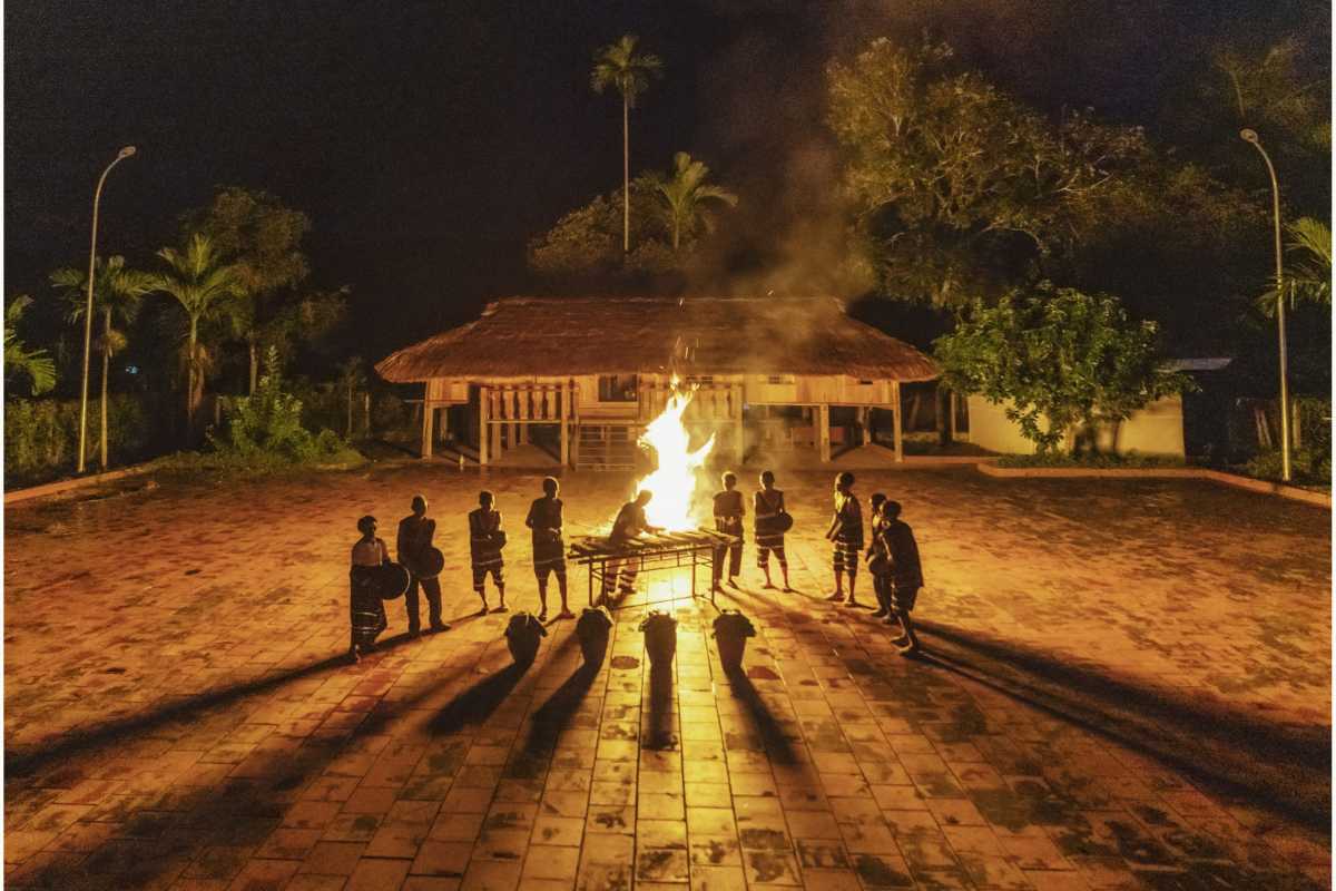 Night bonfire ceremony People dressed in tribal clothes stand around a blazing bonfire near a stilt house in the Cai River region.