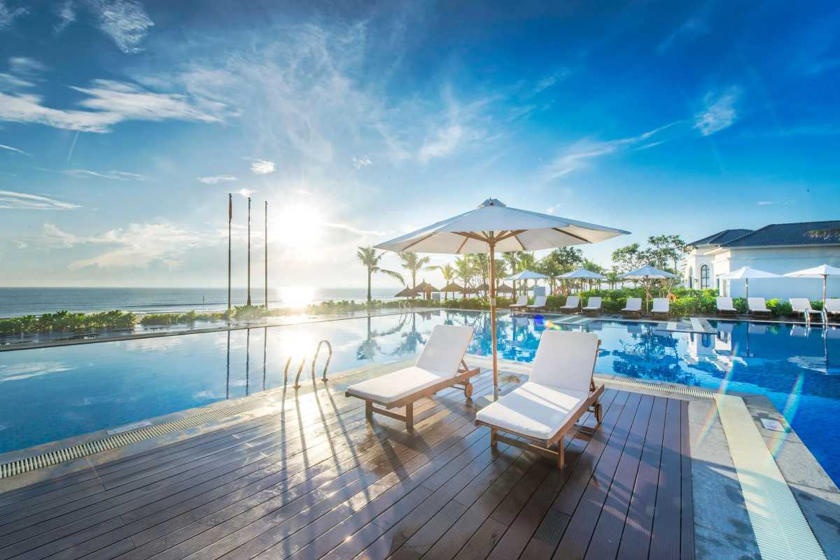 Non Nuoc Beach Da Nang luxury poolside sunrise view Non Nuoc Beach Da Nang luxury resort pool overlooks the sea with sun loungers and umbrellas at sunrise for a tranquil morning experience.