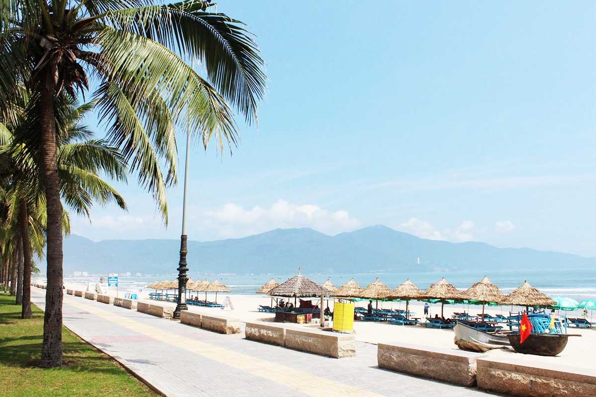 Non Nuoc Beach Da Nang palm-fringed promenade and beach huts Non Nuoc Beach Da Nang palm-lined promenade offers beach huts, sun loungers, and panoramic ocean views under a clear blue sky.
