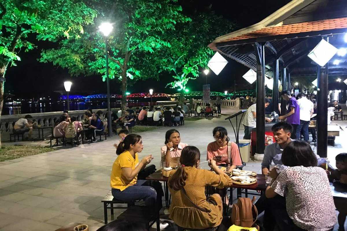 Outdoor Seating Along Nguyen Dinh Chieu Walking Street Groups of people dining at outdoor tables with colorful lanterns and the Perfume River in the background
