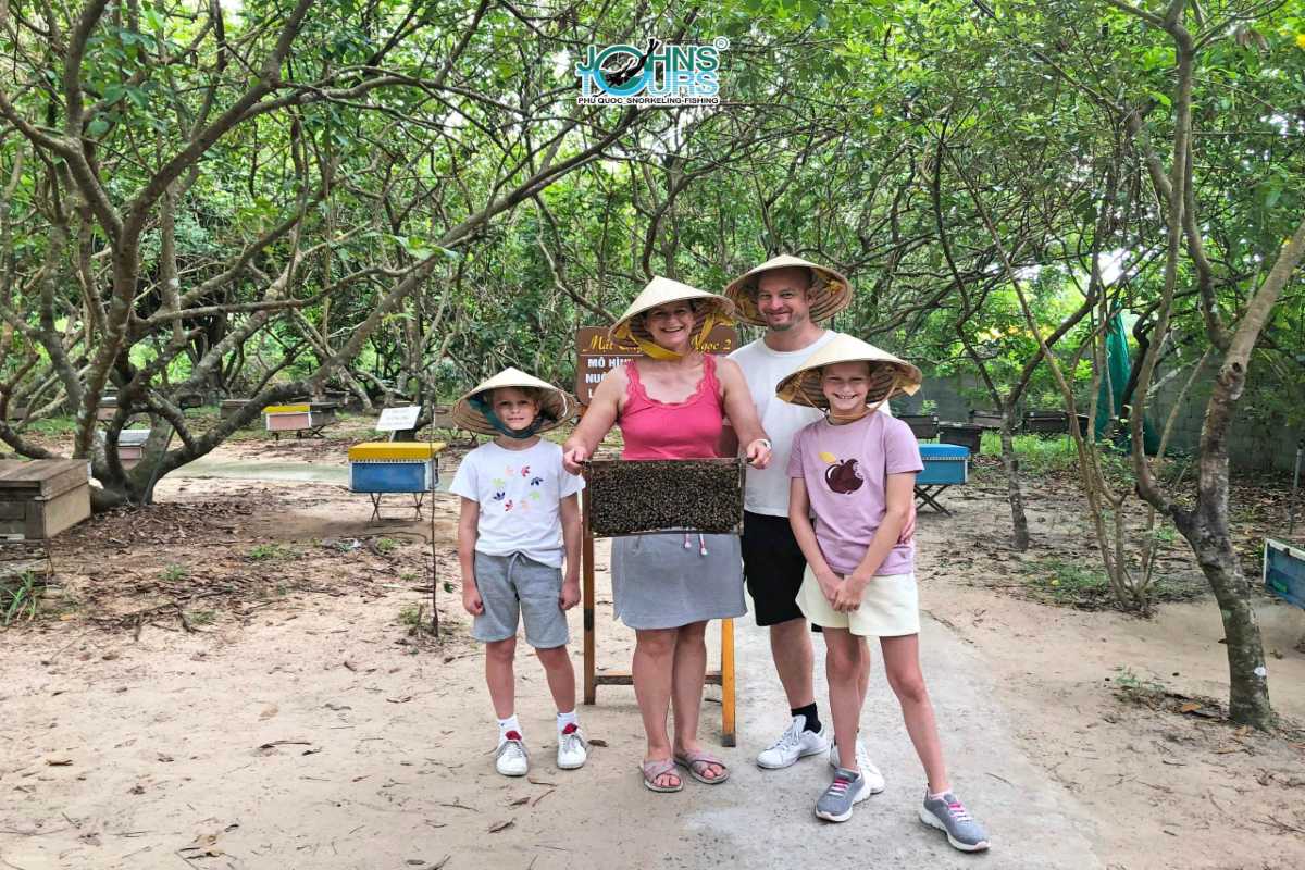 Happy family enjoying bee farm visit at Phu Quoc Bee Farm Smiling family wearing hats and holding honeycomb frame at Phu Quoc Bee Farm