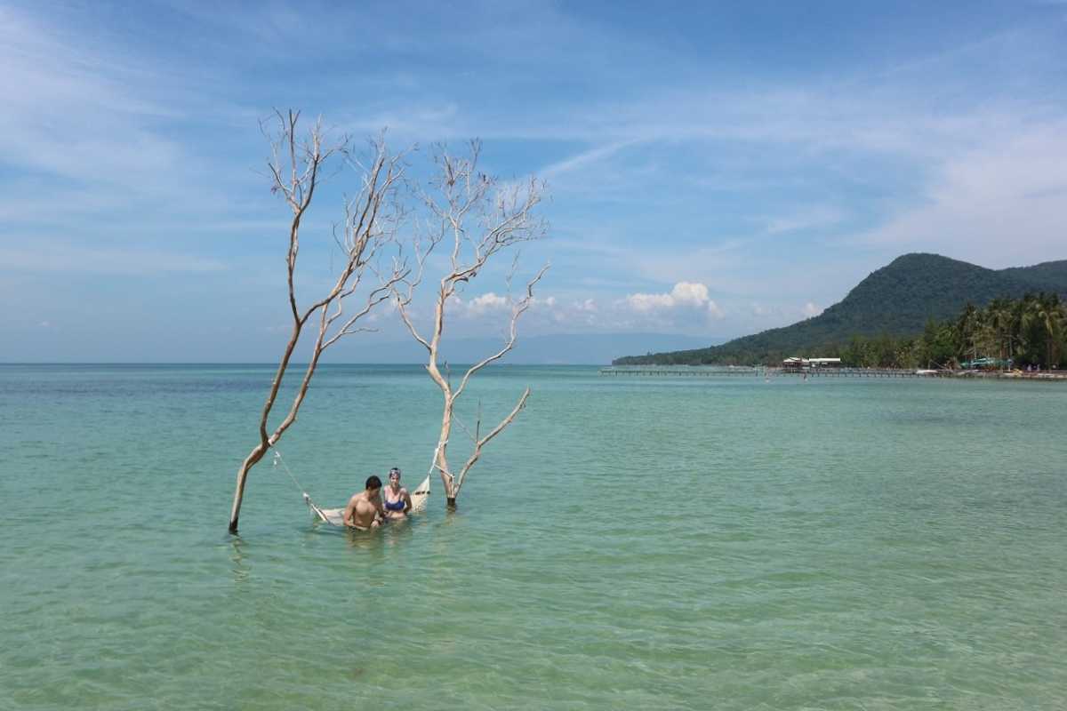 Clear turquoise waters and palm-fringed white sandy beach at Phu Quoc Island with boats anchored near shore.