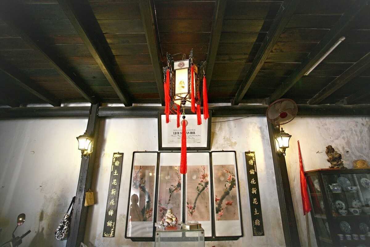 Ceiling Detail with Lantern – Phung Hung Ancient House Lantern with red tassels hanging from wooden ceiling inside Phung Hung House, surrounded by traditional wall scrolls.