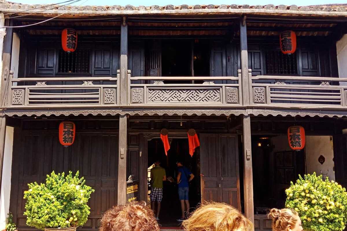 Visitors at Entrance – Phung Hung Ancient House Hoi An Tourists entering Phung Hung Ancient House in Hoi An through its dark timber façade and red lantern-marked entrance.