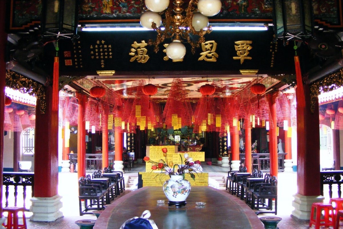 Interior view of Quan Cong Temple in Hoi An showcasing traditional Confucian architecture and red columns with incense spirals hanging above.