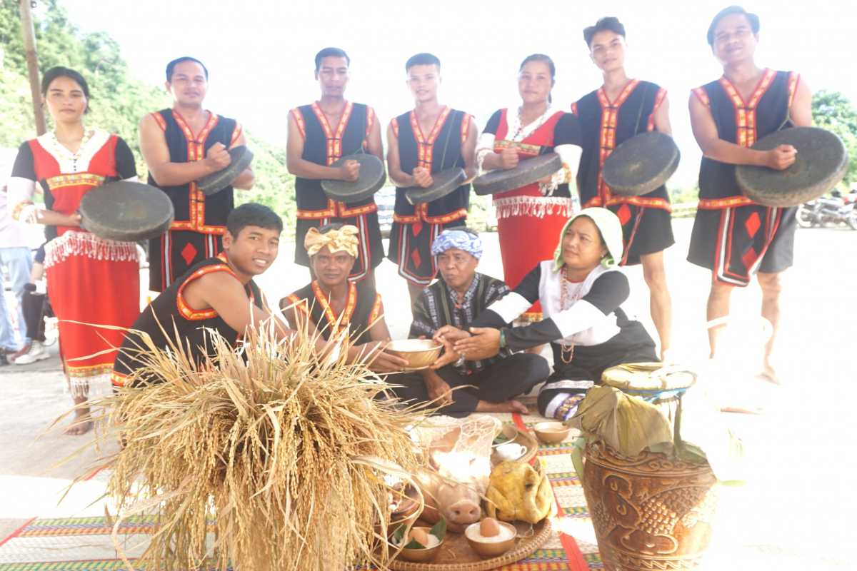 Raglai villagers in traditional dress perform a harvest ceremony with gongs, rice bundles, and ceremonial offerings.