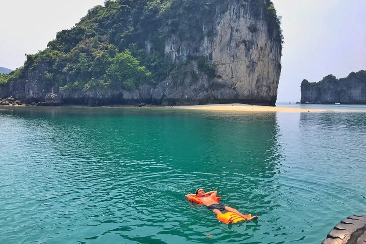 A traveler floating on tranquil waters at Tra Bau in Lan Ha Bay, surrounded by limestone cliffs.