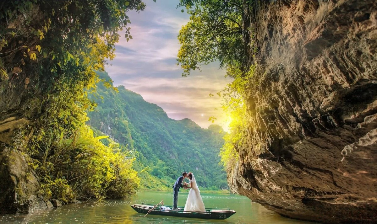 Couple on a boat ride in Am Tien Cave surrounded by limestone cliffs at sunset