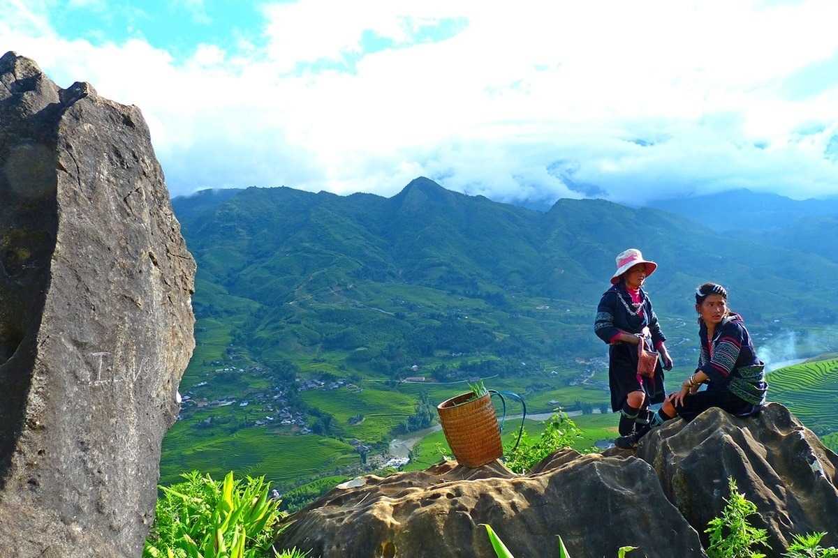 Sapa Heaven Gate Hmong women mountain vista cultural view Hmong women in traditional dress at Sapa Heaven Gate, sitting on rocks with terraced valley in background