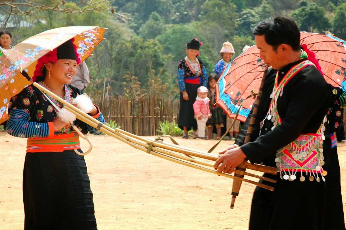 Sapa Love Market daytime umbrella courtship ritual with ethnic couple Sapa Love Market displays a daytime scene with an ethnic couple performing the traditional umbrella courtship ritual in Sapa.
