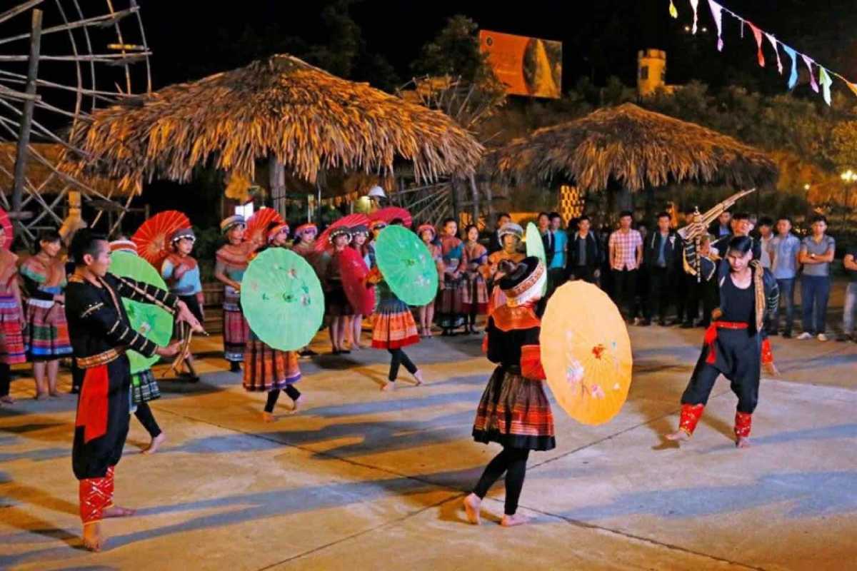 Sapa Love Market umbrella dance performance with ethnic costumes Sapa Love Market performers in traditional ethnic costumes present a lively umbrella dance under thatched roofs at night.