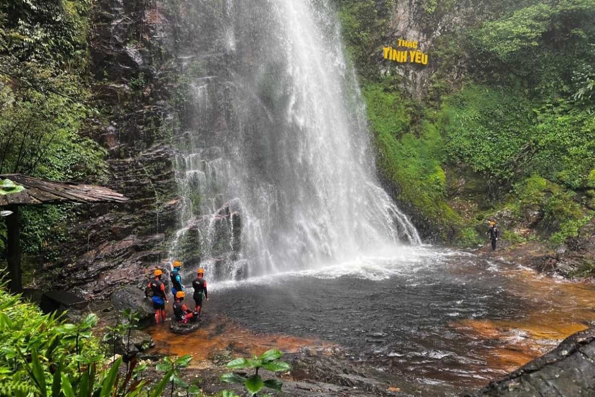 Sapa Love Waterfall base group adventure Adventurers with helmets stand at the base pool of Sapa Love Waterfall, surrounded by mist and lush greenery in Sapa.