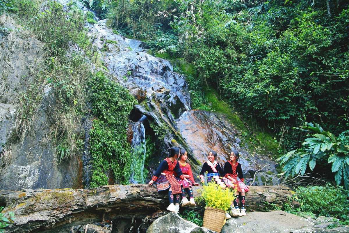 Sapa Love Waterfall ethnic girls near small falls Ethnic minority girls in colorful dress relax by a small waterfall and log in Sapa’s lush green forest