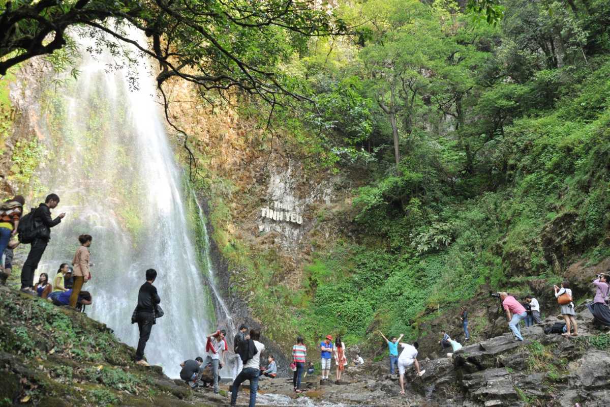 Sapa Love Waterfall popular viewpoint travelers gather Groups of visitors gather at a popular viewpoint beside Sapa Love Waterfall, surrounded by green forest and rocky slopes.