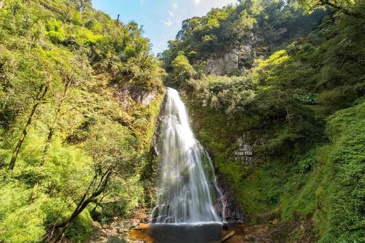 Sapa Love Waterfall vertical cascade sunny day Sunlight illuminates Sapa Love Waterfall as water falls straight down into a forested clearing below