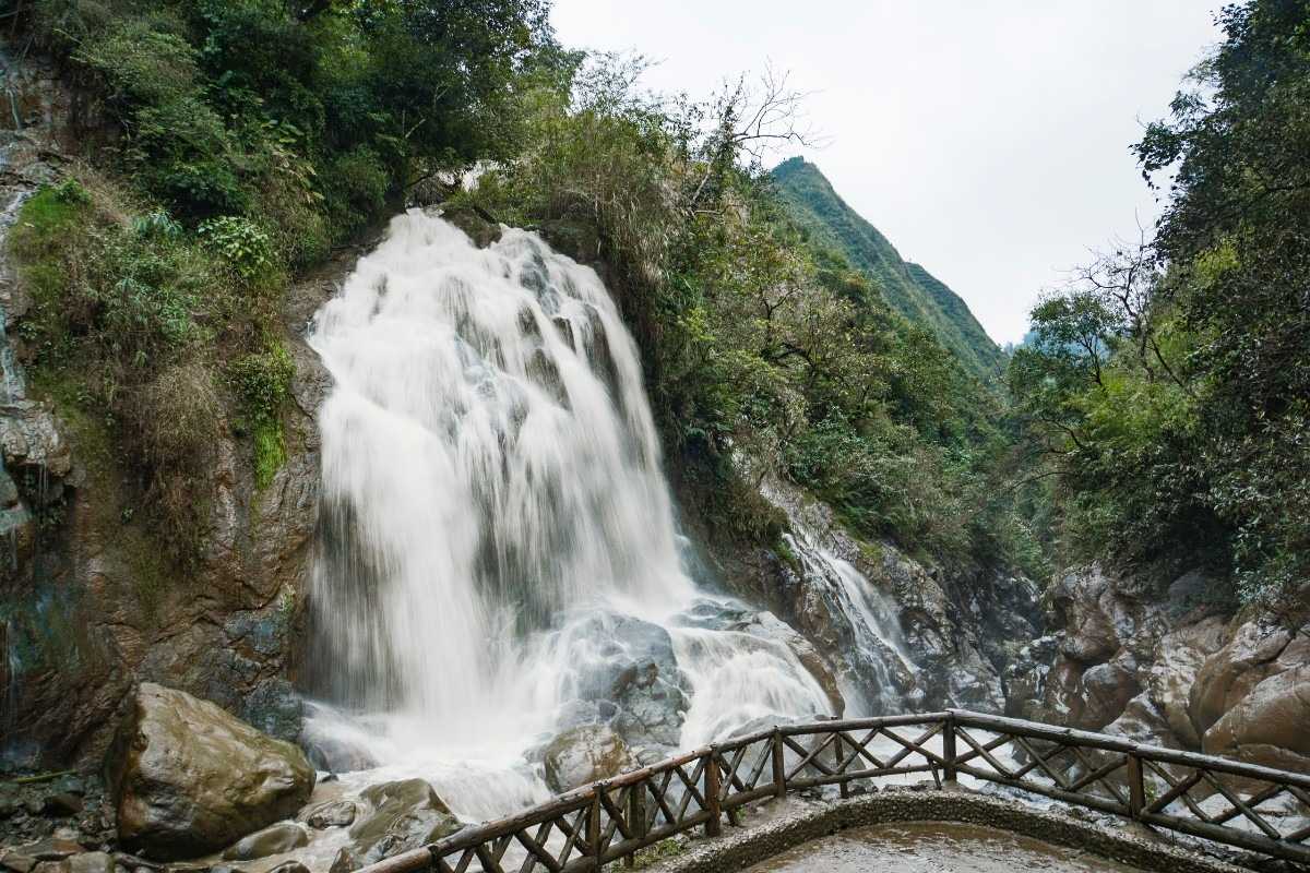 Sapa Love Waterfall wooden fence and foamy drop Sapa Love Waterfall plunges over rocks behind a rustic wooden fence, surrounded by greenery and clear water