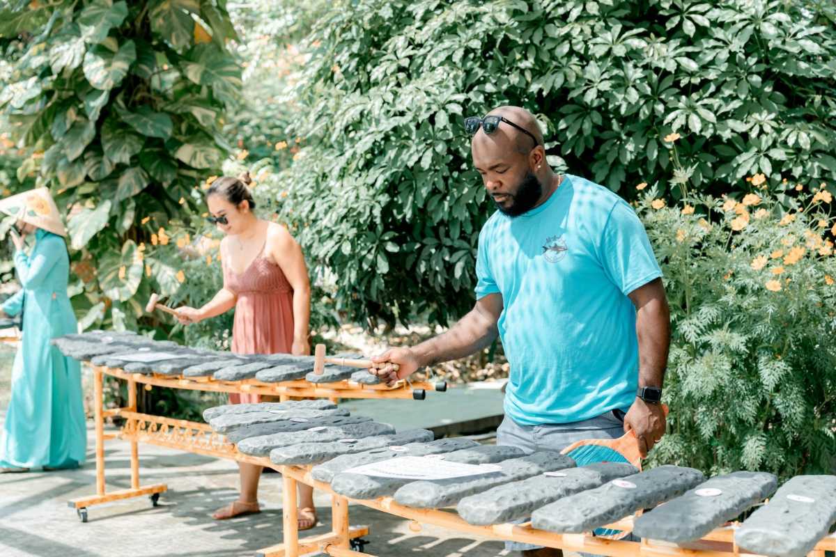Visitors Playing Stone Instruments Tourists playing traditional stone xylophones in a lush outdoor setting during a Cai River cultural tour in Nha Trang.