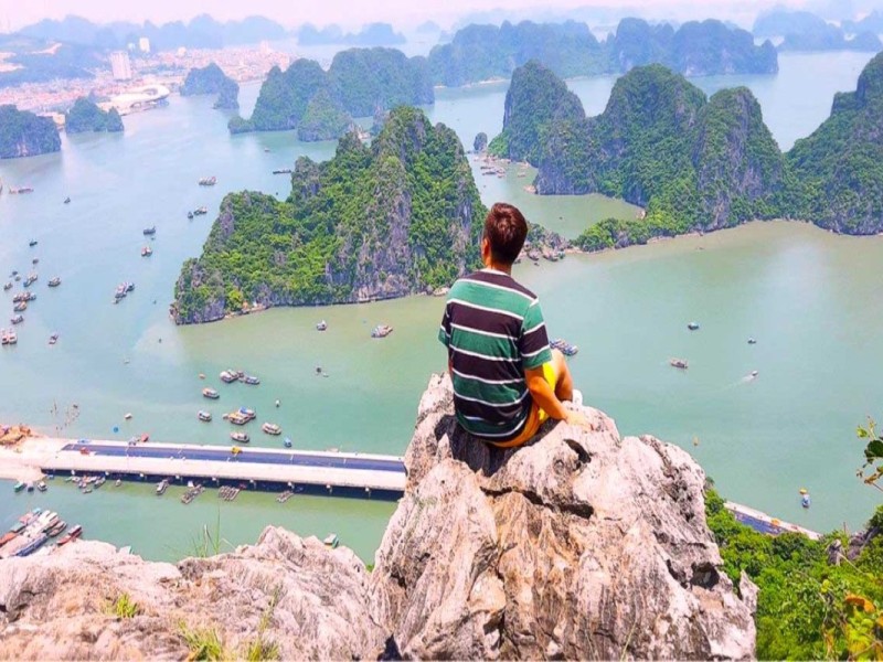 A breathtaking view of Halong Bay with limestone islands, a man sitting on a rock overlooking the bay.