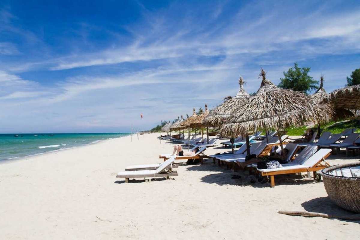 Sun Loungers and Palm-Fringed Shore at Cua Dai Beach Row of sun loungers with thatched umbrellas along the white sand of Cua Dai Beach under bright skies