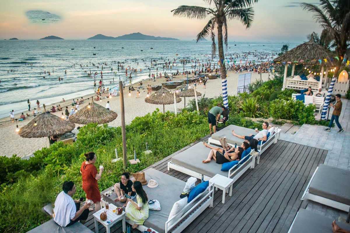 Sunset Gathering at An Bang Beach People relaxing and dining on beachside loungers with palm trees and sunset over the ocean