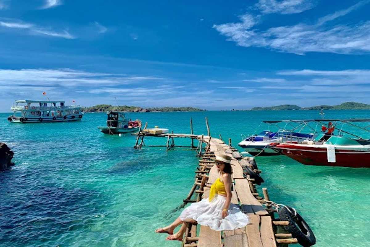 Wooden jetty leading to boats on turquoise water at Sunset Sanato Phu Quoc Island coastal beach
