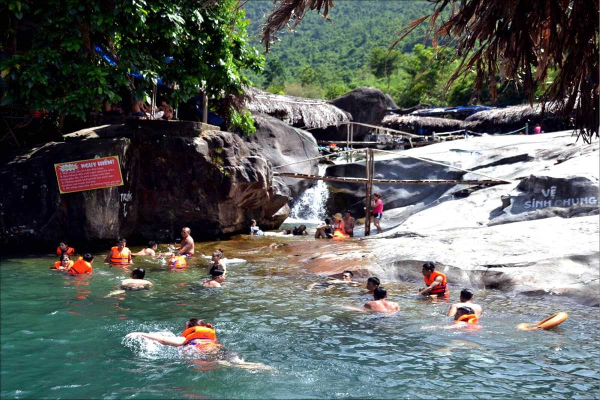 Swimming area and lifeguard signs at Elephant Springs Tourists swimming with life jackets in deep spring pools beside safety signs and rocks at Elephant Springs in Hue