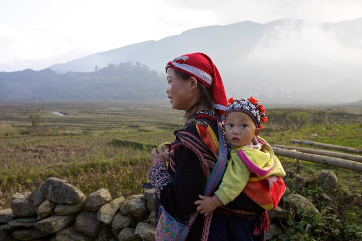 Ta Phin Village Sapa Red Dao woman and child traditional attire Ta Phin Village Sapa shows a Red Dao woman with her baby, wearing traditional clothing and headscarves in open countryside