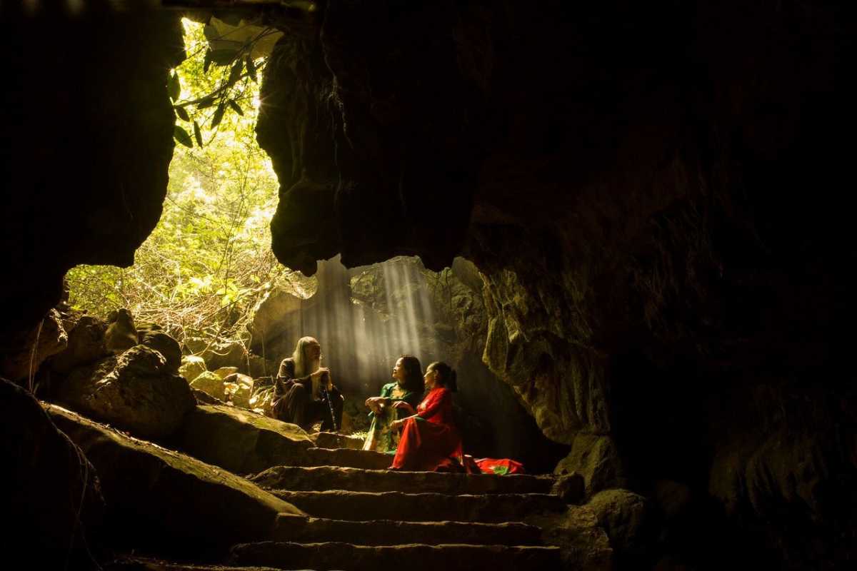 Thien Ha Cave Ninh Binh group resting in cave opening Group of visitors resting inside the entrance of Thien Ha Cave Ninh Binh, sunlight filtering through lush forest outside.