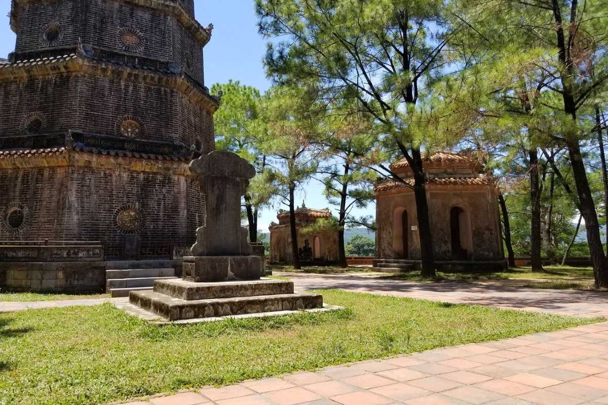Thien Mu Pagoda brick tower and ancient steles in Hue Thien Mu Pagoda brick tower and stone stele with pine trees, representing the tranquil Buddhist heritage of Hue’s iconic landmark.