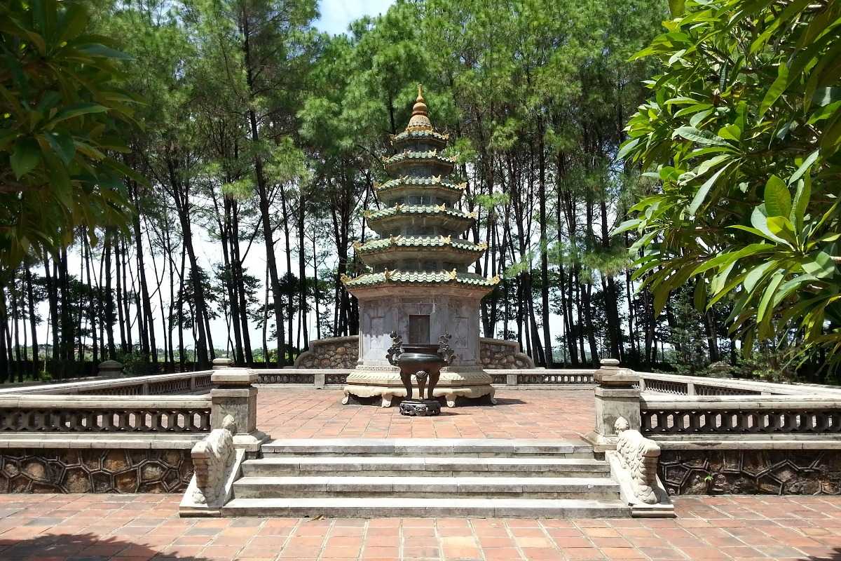 Pagoda stupa and pine forest at Thien Mu Pagoda grounds in Hue Stupa rises at Thien Mu Pagoda amid tall pine trees, with ceremonial incense burner and peaceful tiled courtyard, reflecting the pagoda’s tranquil setting.