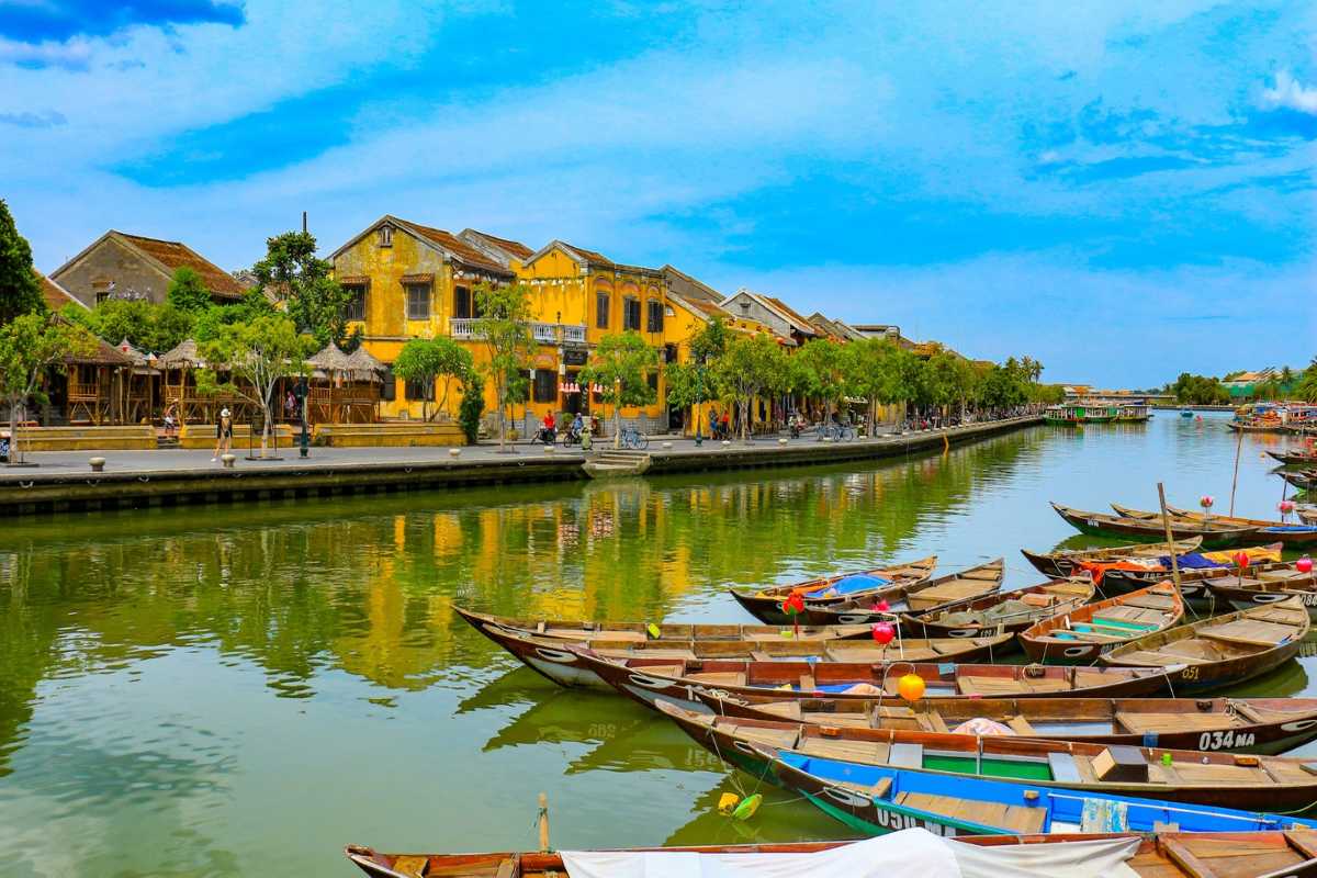 Scenic View of Thu Bon River and Hoi An Riverside Traditional boats docked on Thu Bon River with yellow colonial houses lining riverbank