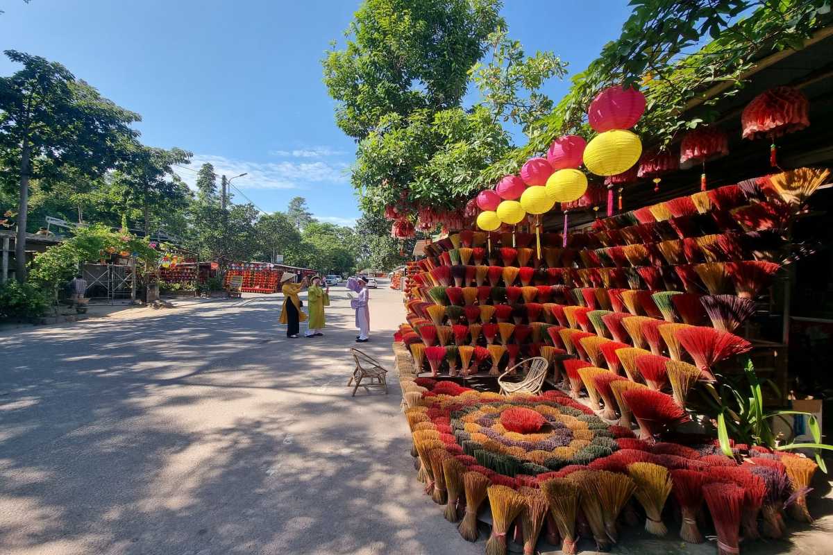 Main Street Scene at Thuy Xuan Incense Village Hue Visitors in ao dai and traditional hats stroll along incense-lined main street at Thuy Xuan Incense Village in Hue.