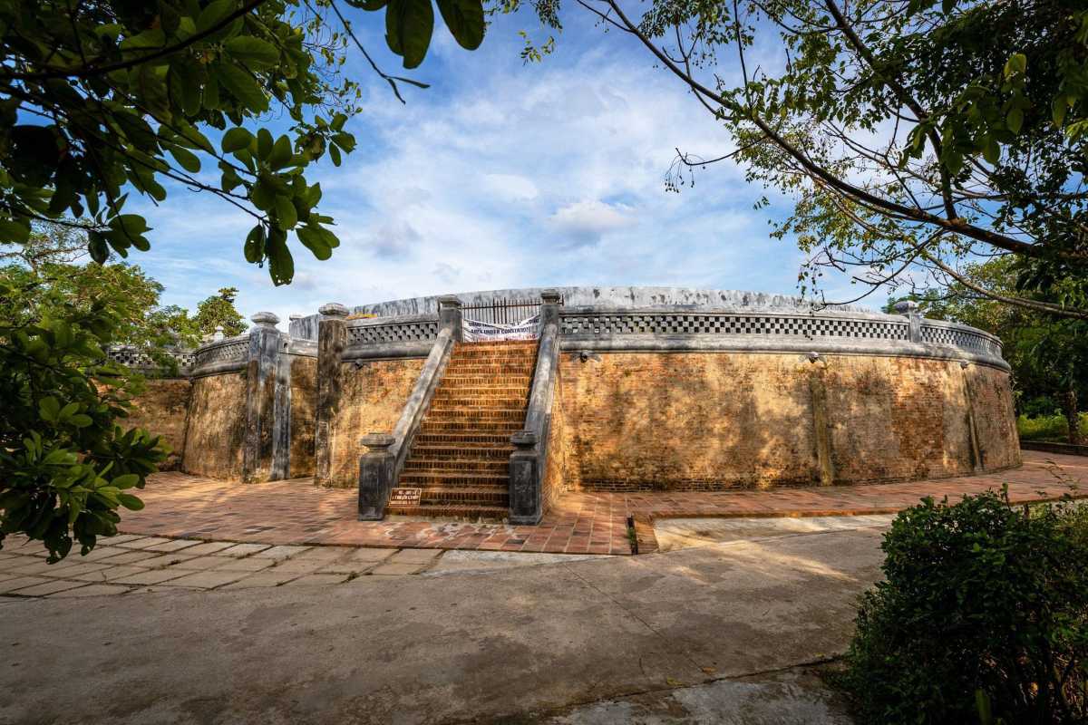 Tiger Arena Hue side staircase and curved exterior under blue sky Tiger Arena Hue features a wide stone staircase rising alongside the arena’s curved outer wall, beneath a clear blue sky and greenery.