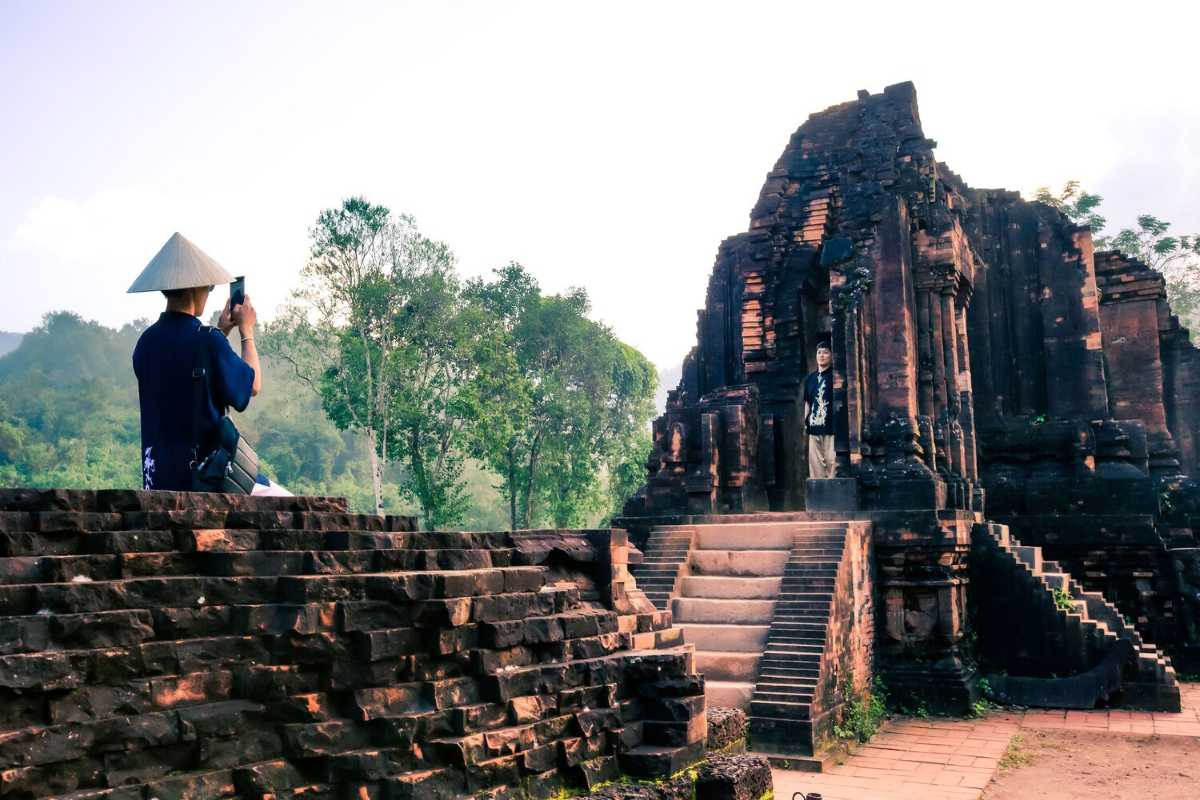 Tourist Walking Among My Son Sanctuary Ruins Visitors exploring the pathways among ancient temples at My Son Sanctuary under bright daylight