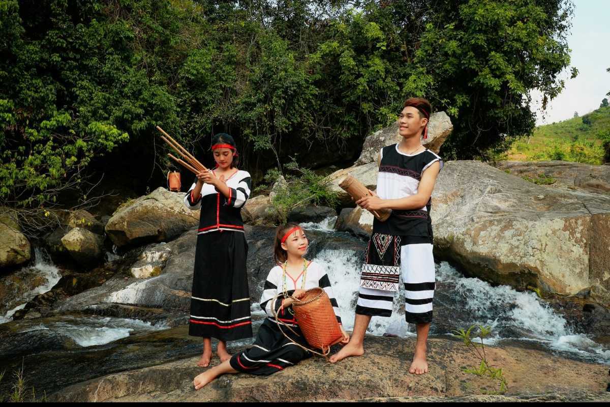 Three young ethnic people in traditional dress pose near a rocky stream along the Cai River in Nha Trang.