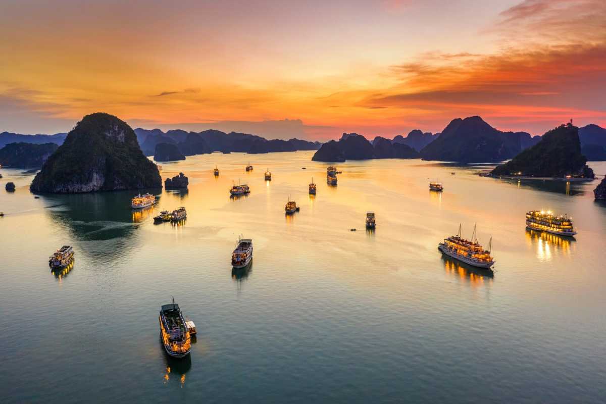 Traditional Halong Bay cruise with orange sails A traditional cruise boat with orange sails glides through green waters of Halong Bay during sunset.