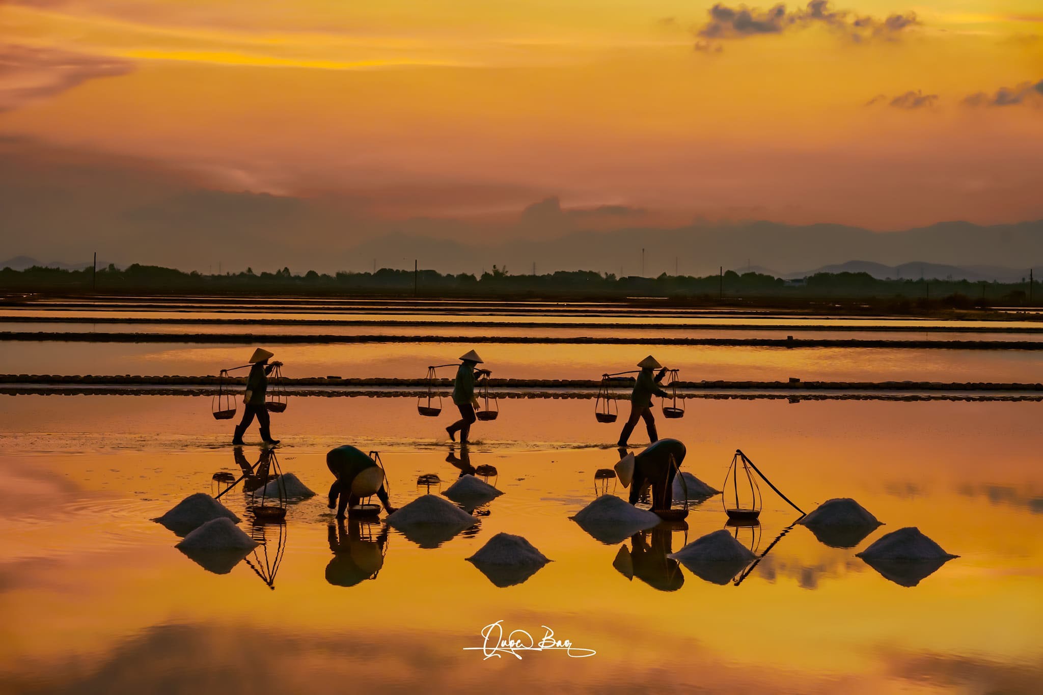 Traditional Salt Harvesting in Hon Khoi Commune Workers in conical hats harvesting salt in Hon Khoi Commune under a golden sunset sky