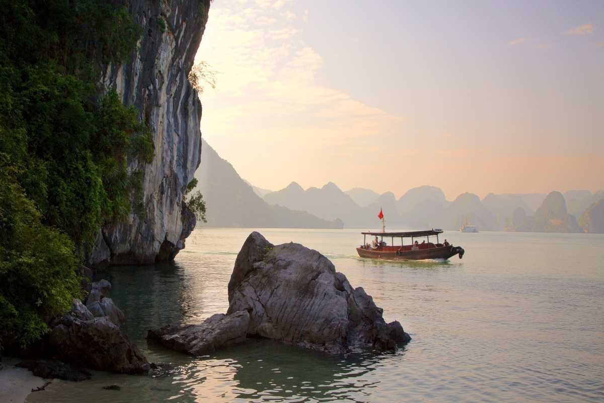 Traditional Wooden Boat Passing Soi Sim Island Traditional Vietnamese wooden boat sailing past limestone cliffs near Soi Sim Island Halong Bay