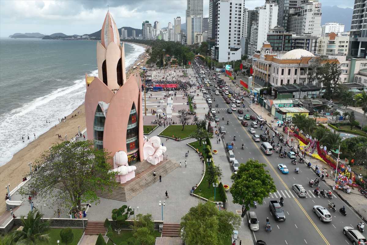 Aerial view of Tram Huong Tower beside Nha Trang Beach with busy coastal traffic and crowds gathering nearby