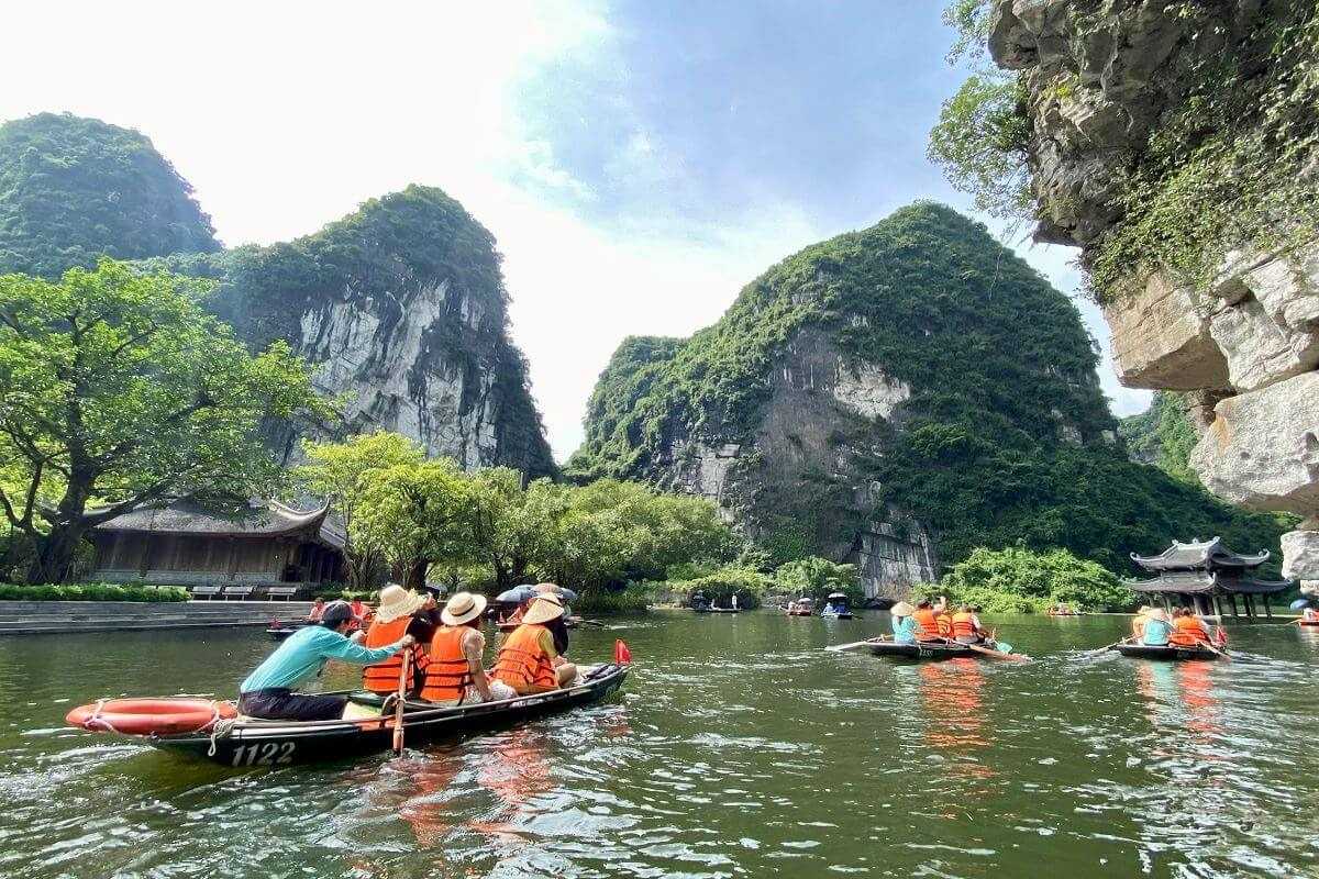Trang An Ninh Binh lively boat tours in lush valley Numerous boat tours navigating the green river valley amid towering limestone hills at Trang An Ninh Binh during peak season.