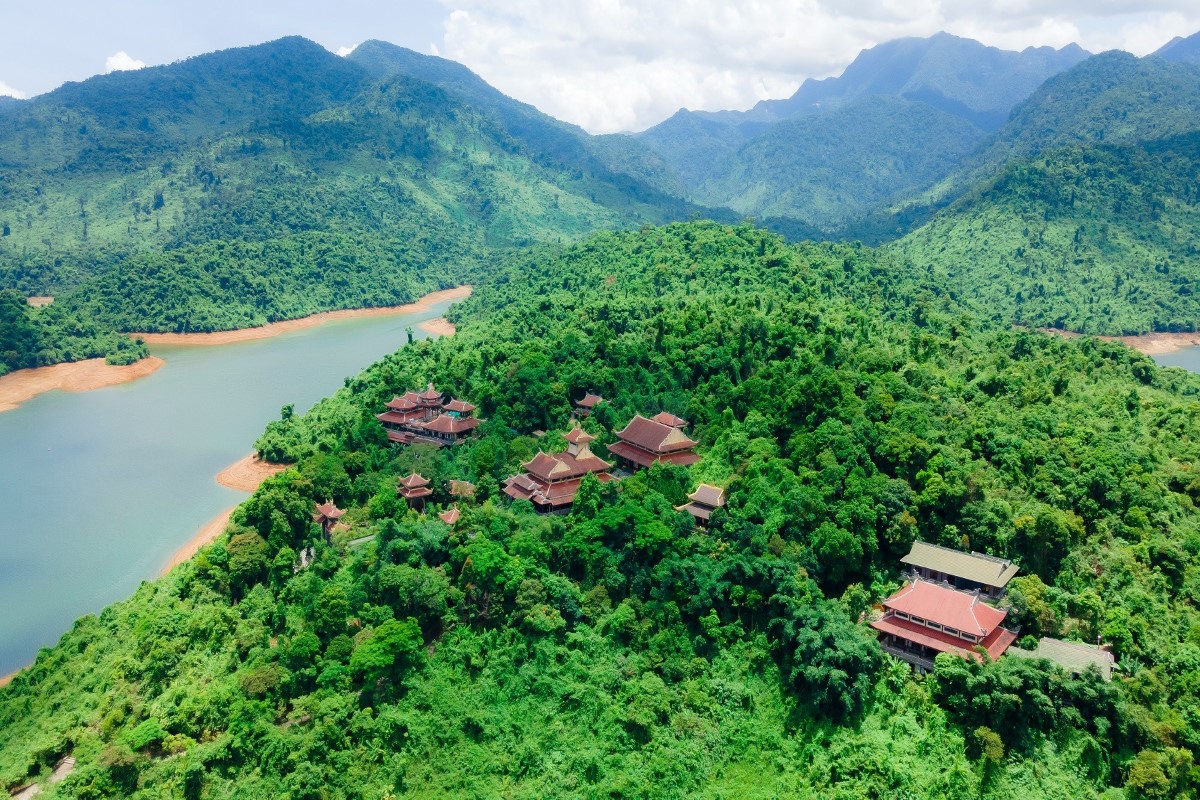 Aerial view of Truc Lam Bach Ma Zen Monastery surrounded by lush green mountains and Truoi Lake