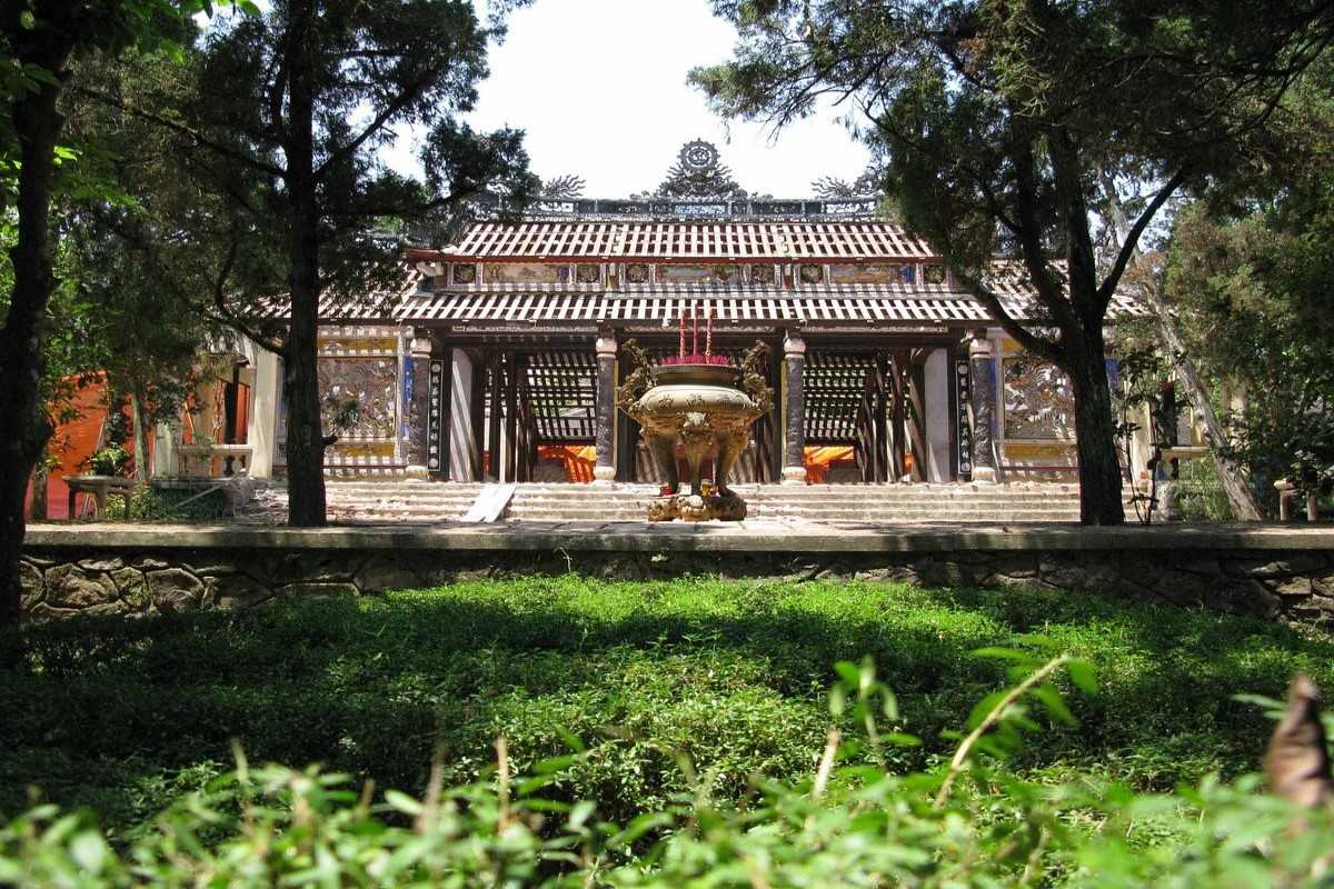 Central Altar of Tu Hieu Pagoda Stone incense urn placed in front of the central altar hall of Tu Hieu Pagoda, shaded by pine trees.