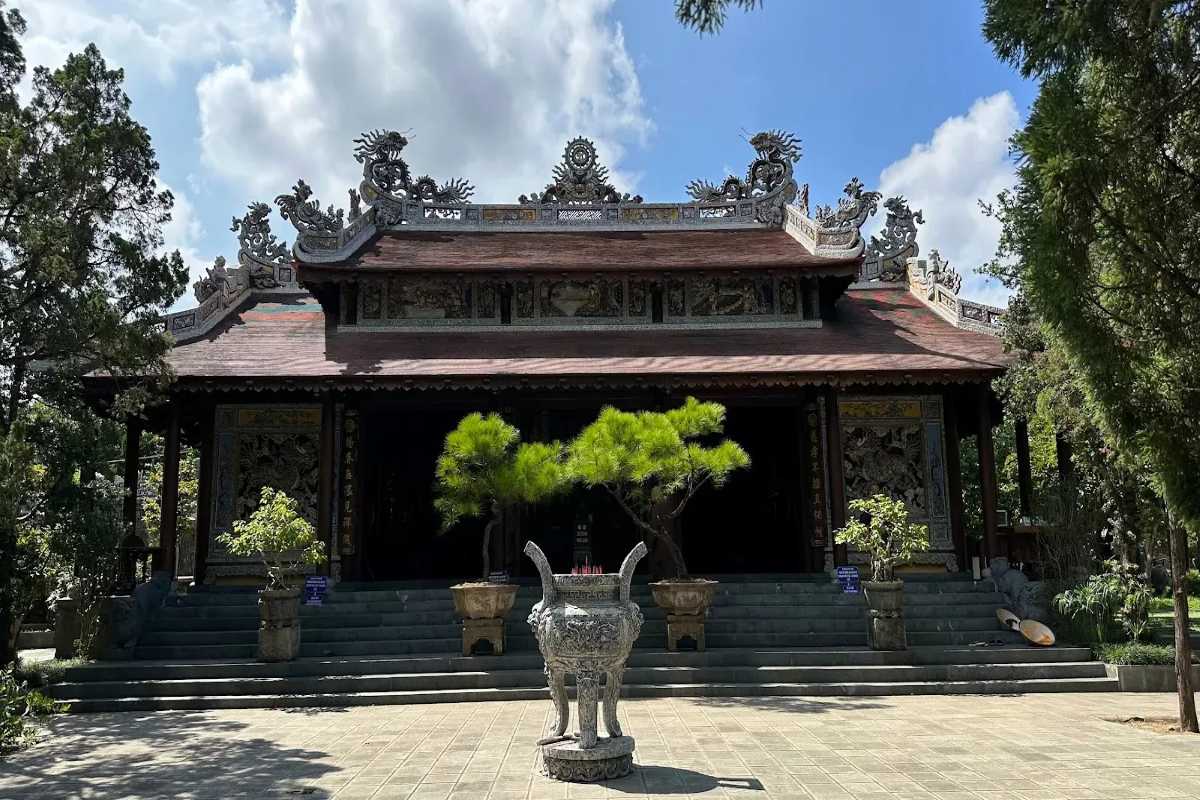 Front view of Tu Hieu Pagoda's main hall with intricate dragon motifs on the roof and incense urn in foreground.