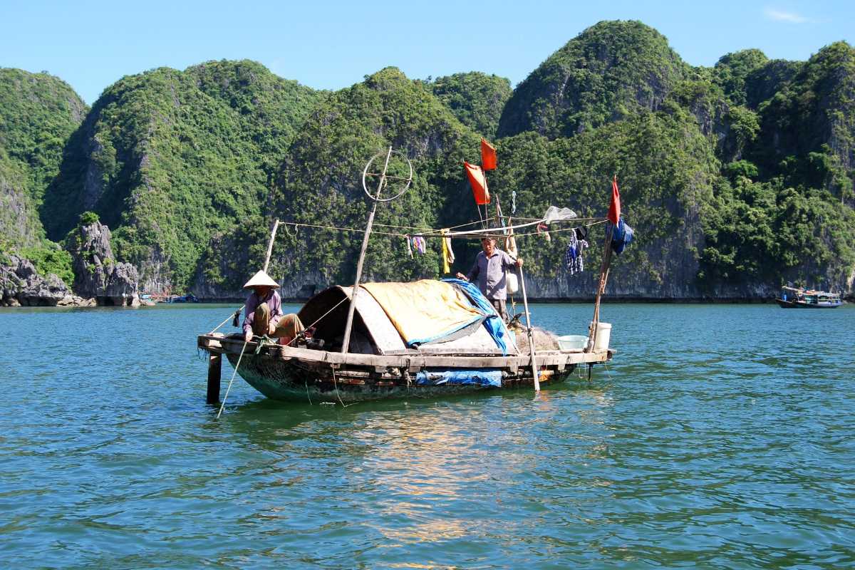 Tourists enjoying boat ride at Tung Sau Pearl Farm Halong Bay Tourists wearing life jackets on small boats at Tung Sau Pearl Farm Halong Bay with towering limestone cliffs in the background